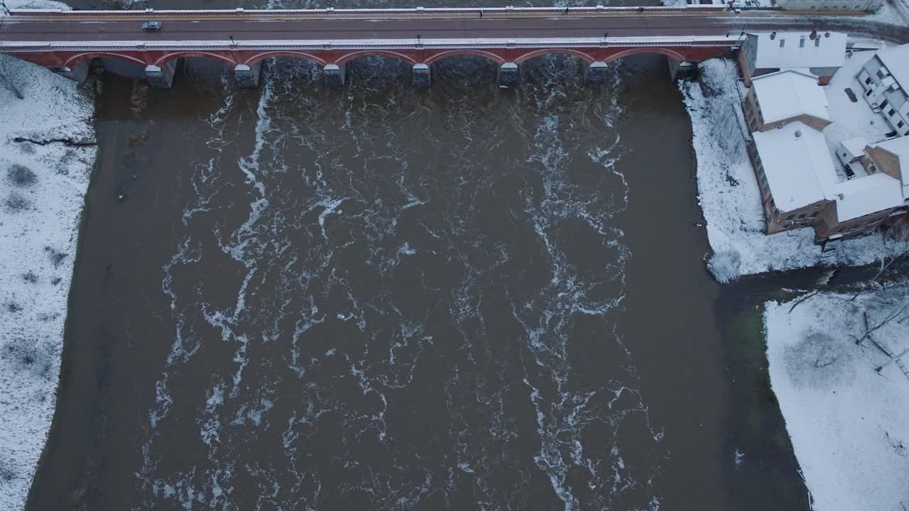 vista aérea de los rápidos del río venta durante la inundación de invierno, viejo puente de ladrillo rojo, kuldiga, letonia, día de invierno nublado, amplia toma de avión no tripulado de ojo de pájaro avanzando