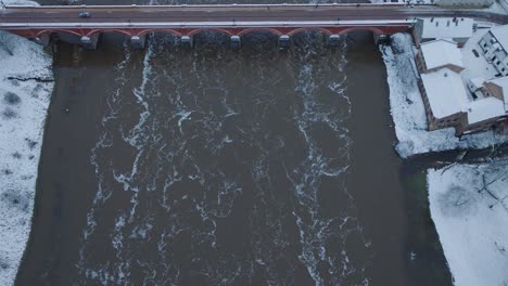 aerial establishing view of venta river rapids during winter flood, old red brick bridge, kuldiga, latvia, overcast winter day, wide birdseye drone shot moving forward