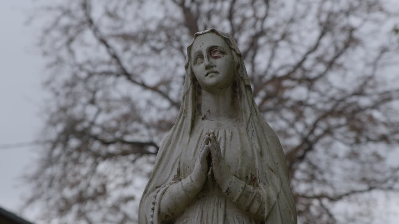 Estátua religiosa desgastada da Virgem Maria em mármore, em cenário natural ao ar livre. Close-up.