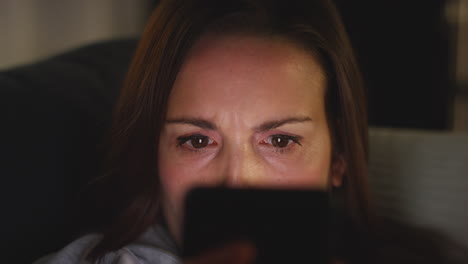 un primer plano de una mujer ansiosa sentada en el sofá de su casa por la noche mirando su teléfono móvil preocupada por las redes sociales o las malas noticias 1