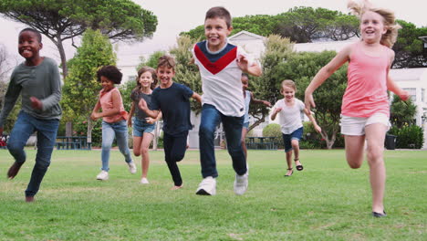 group of excited children playing with friends and running across grass playing field