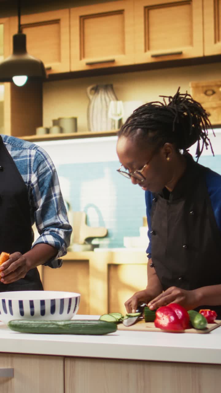 Video verticale di persone afroamericane che tagliano verdure fresche su un tagliere a casa