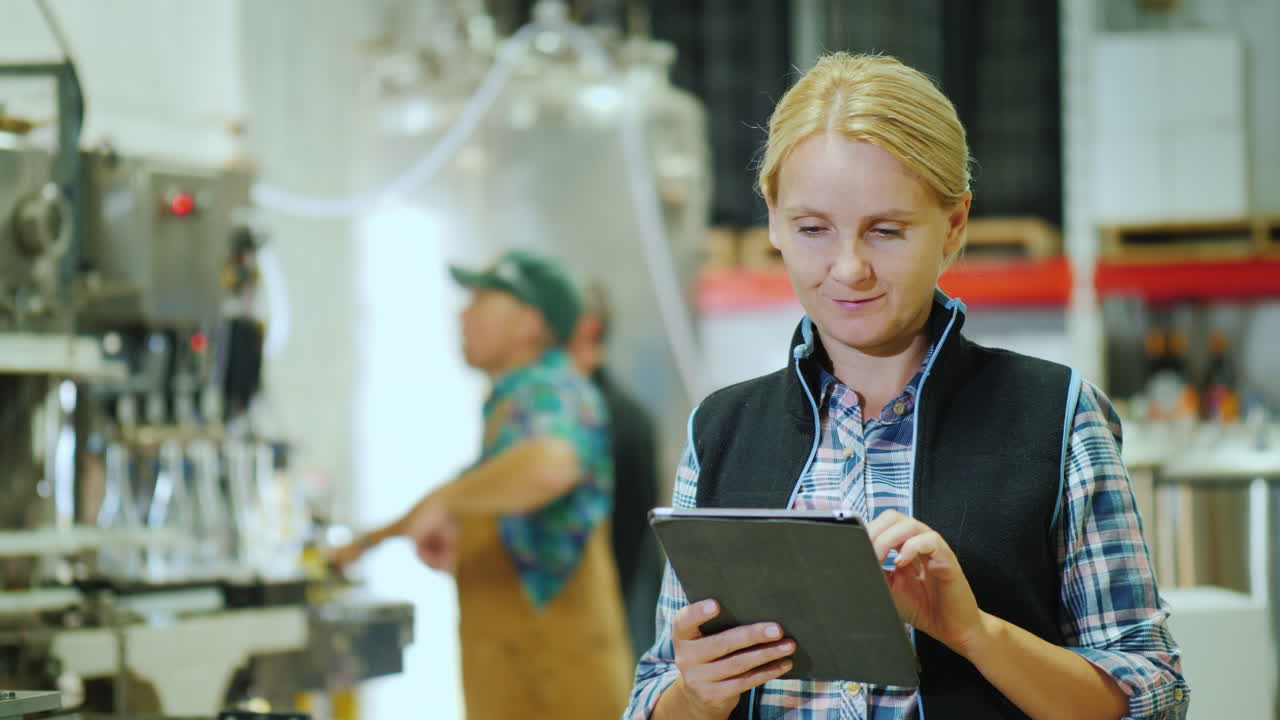 una joven está trabajando con una tableta en el fondo de un transportador para la producción de beverag