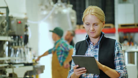 Una-Mujer-Joven-Está-Trabajando-Con-Una-Tableta-En-El-Fondo-De-Un-Transportador-Para-La-Producción-De-Bebidas