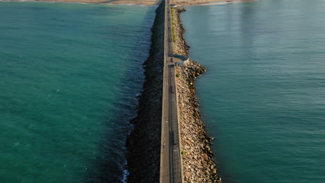 Aerial-view-of-footbridge-with-people-walking-around,-from-the-sea-to-the-city-with-many-buildings-in-the-background,-Fortaleza,-Brazil