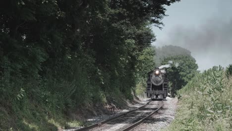 locomotora de vapor vintage acercándose de frente con una cabeza llena de vapor