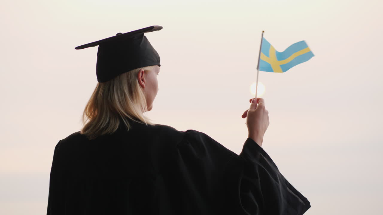 educación en europa - graduado en manto y gorra con bandera de suecia en la mano