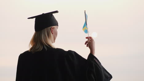 Bildung-In-Europa---Absolvent-In-Mantel-Und-Mütze-Mit-Schwedenflagge-In-Der-Hand