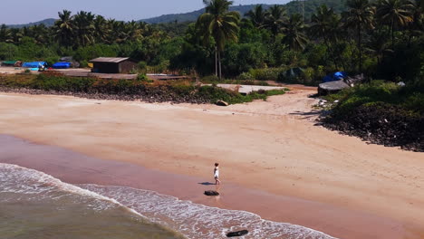 aerial view orbiting a qirl walking on the guhagar beach, in sunny india