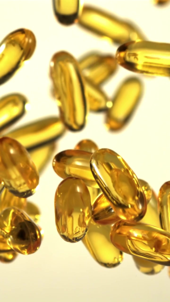 Translucent Golden Capsules Falling and Floating Against White Background