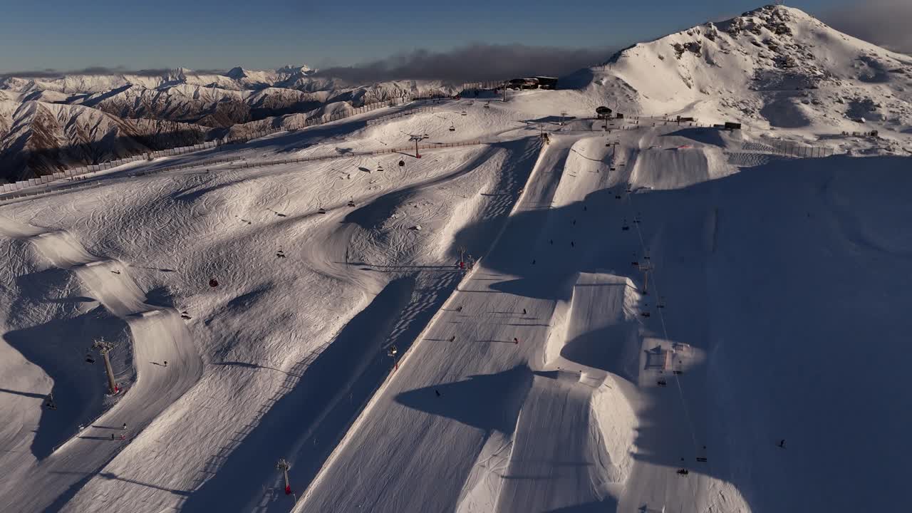 Aerial footage of tourists skiing across the snow-covered peaks of Cardrona Mountain in New Zealand