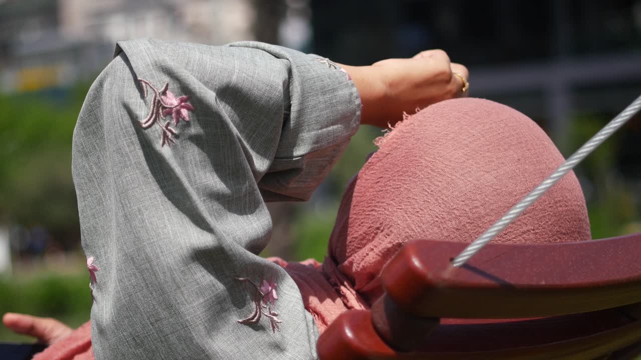 Woman wearing hijab sitting on a swing in a park