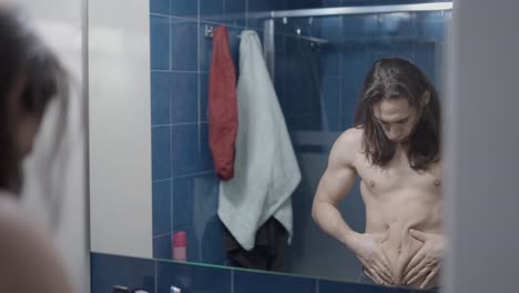 man checking his stomach in the bathroom mirror.