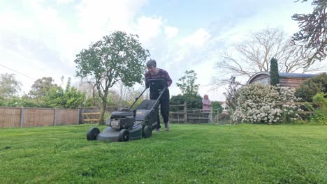 woman pushes lawnmower cutting grass, large garden maintenance