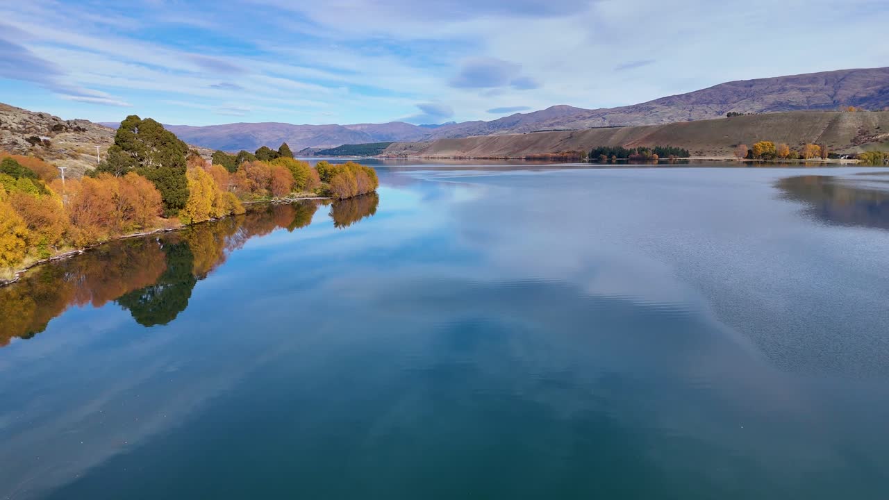 Aerial view of Lake Dunstan with vibrant autumn foliage, clear skies, and calm waters in Cromwell, New Zealand