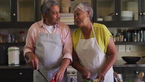 una feliz pareja biracial con delantales preparando comida en la cocina