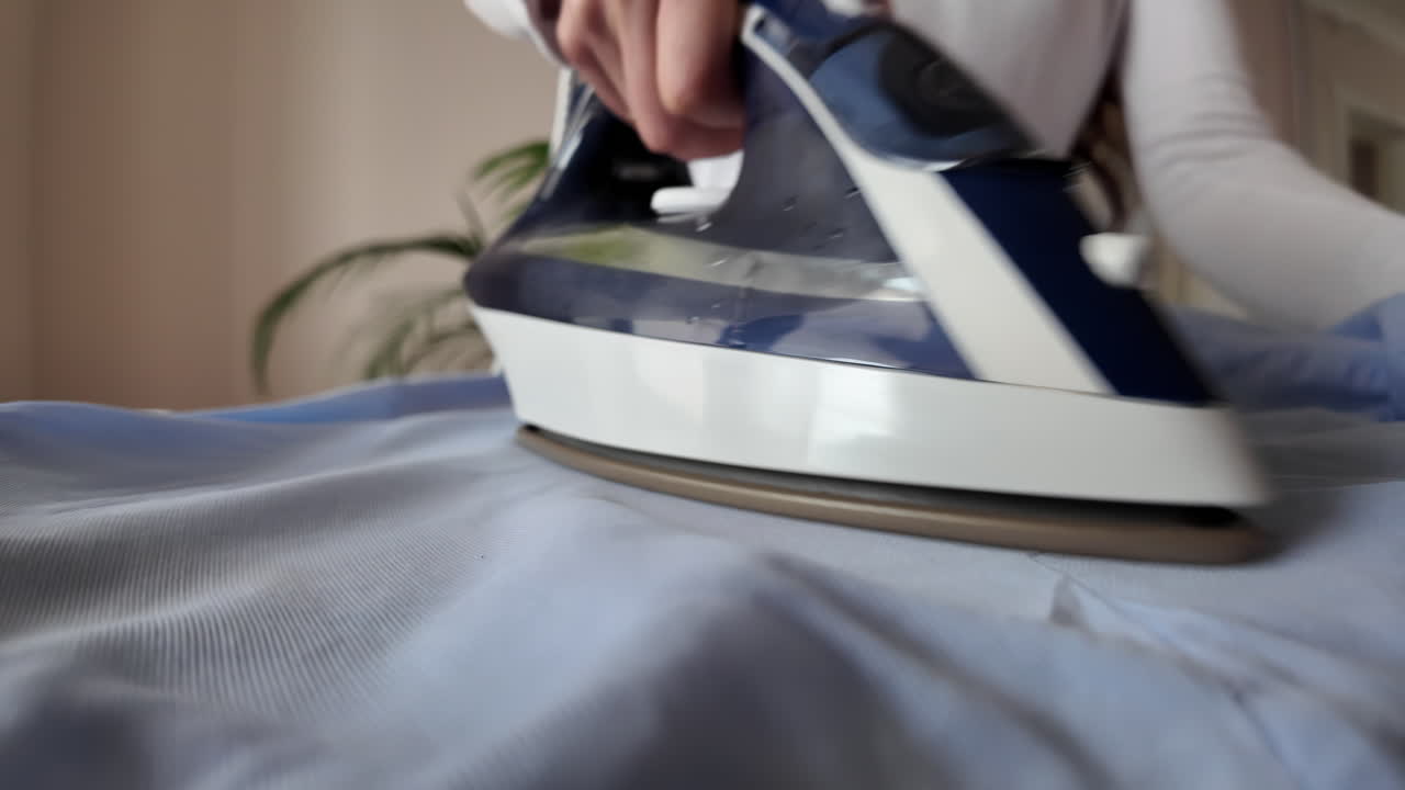 Close up woman ironing a blue shirt at home with white steam