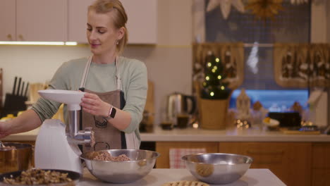 woman prepares holiday dishes grinding meat in meat grinder