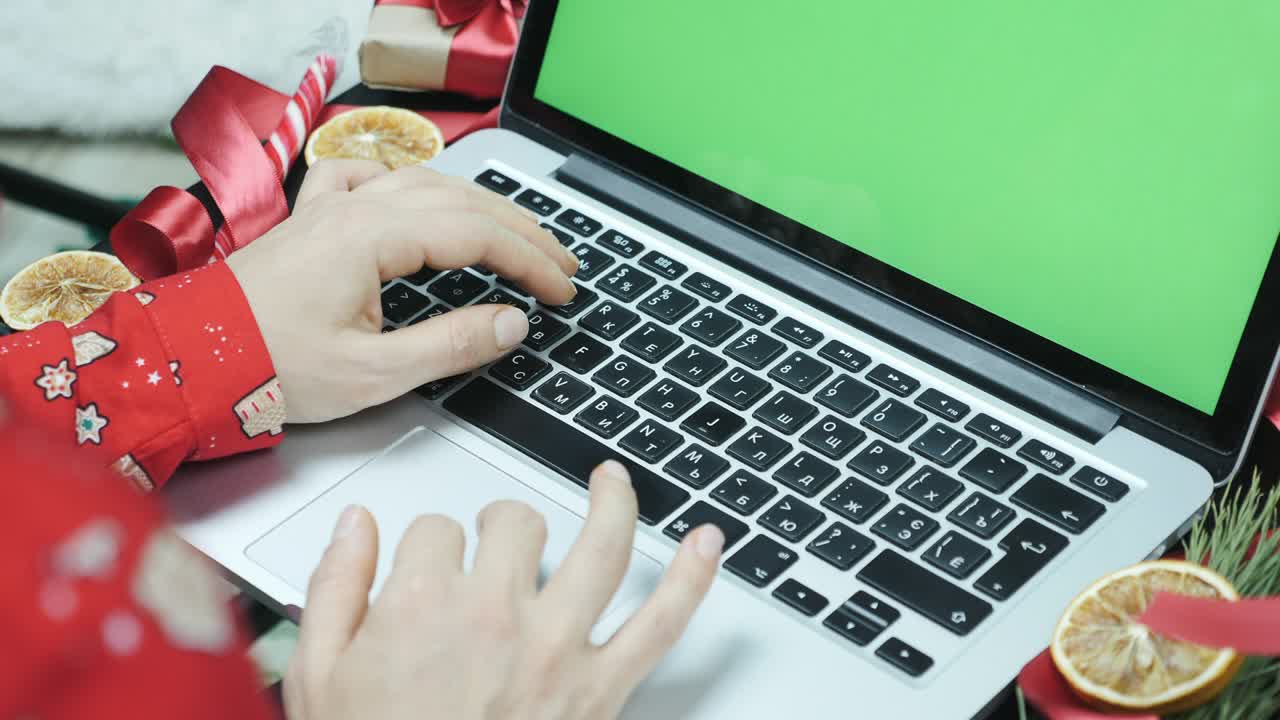 Christmas shopping online at home with laptop with green screen, chromakey. Woman is using laptop near Christmas tree. Woman is using laptop searching for purchasing season sale and christmas presents
