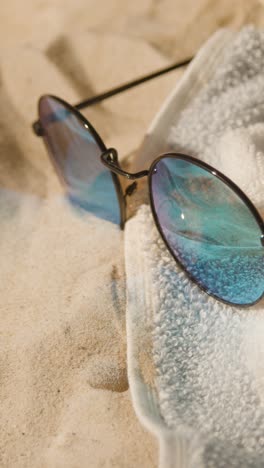 Vertical-Video-Summer-Holiday-Concept-Of-Sunglasses-And-Beach-Towel-On-Sand