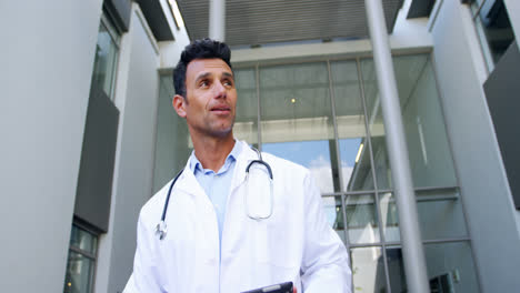 Doctor-holding-digital-tablet-while-walking-in-corridor