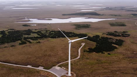 tomada de un avión no tripulado de una turbina eólica escocesa con lagos y páramos detrás de ella