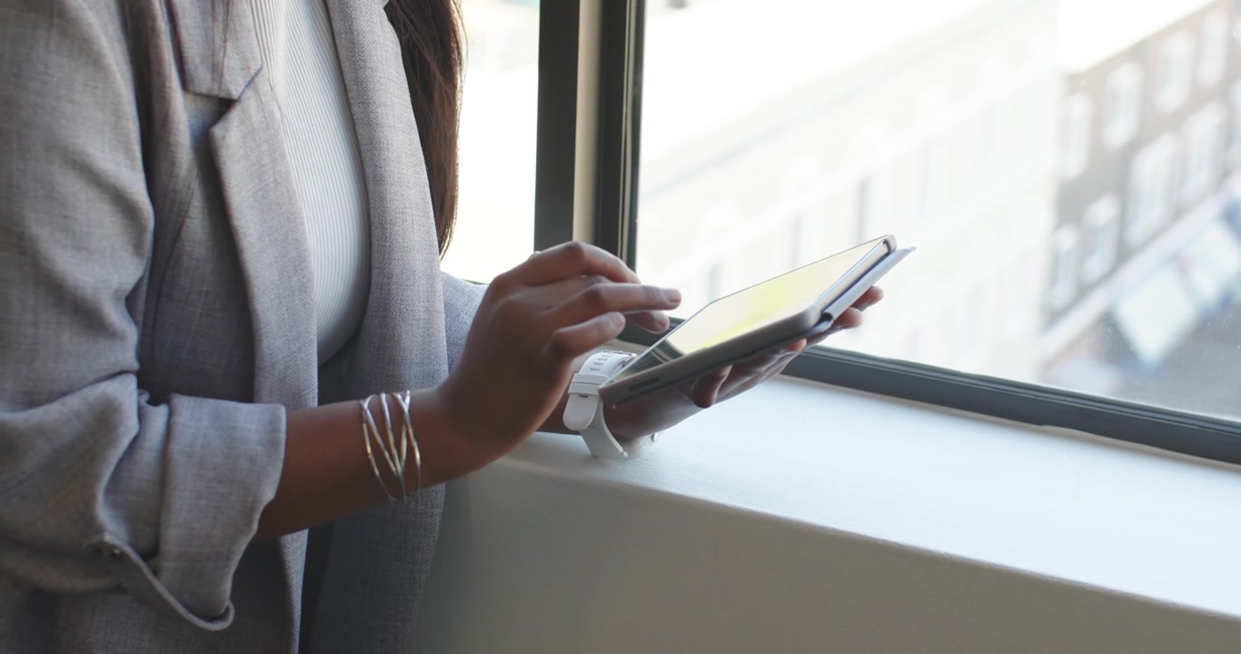 Touching tablet screen on windowsill, woman is tapping and swiping while navigating work apps