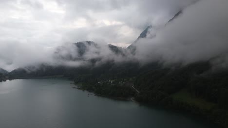 Drone-shot-of-a-Alpine-lake-after-rain-surrounded-by-high-mountains-covered-in-clouds-in-Switzerland-Klontalersee