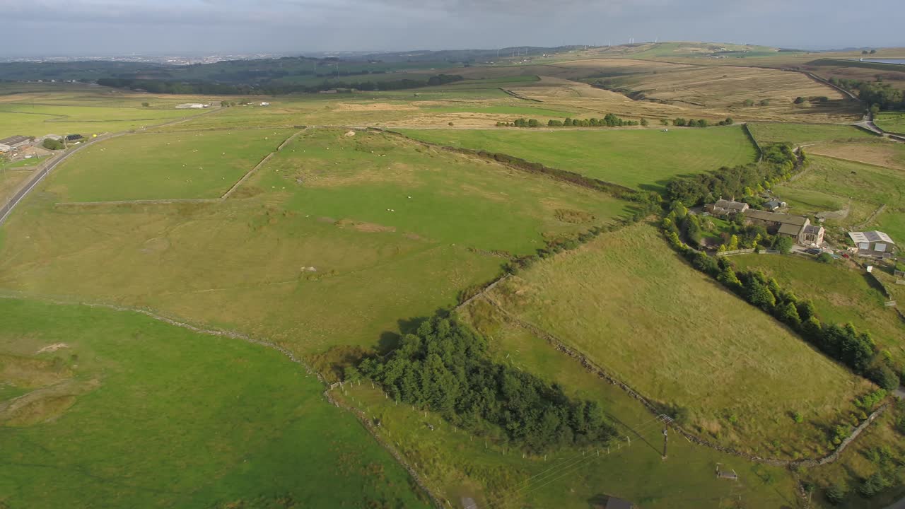 imágenes de drones laterales en la hora dorada de la noche de la zona rural de west yorkshire que muestran tierras de cultivo, páramos, edificios agrícolas, caminos de campo, paredes de piedra seca, ovejas en los campos, árboles y ciudades en la distancia
