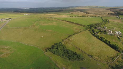 sidewards drone footage at golden hour in the evening of rural west yorkshire showing farmland, moors, farm buildings, country lanes, dry stone walls, sheep in fields, trees and towns in the distance