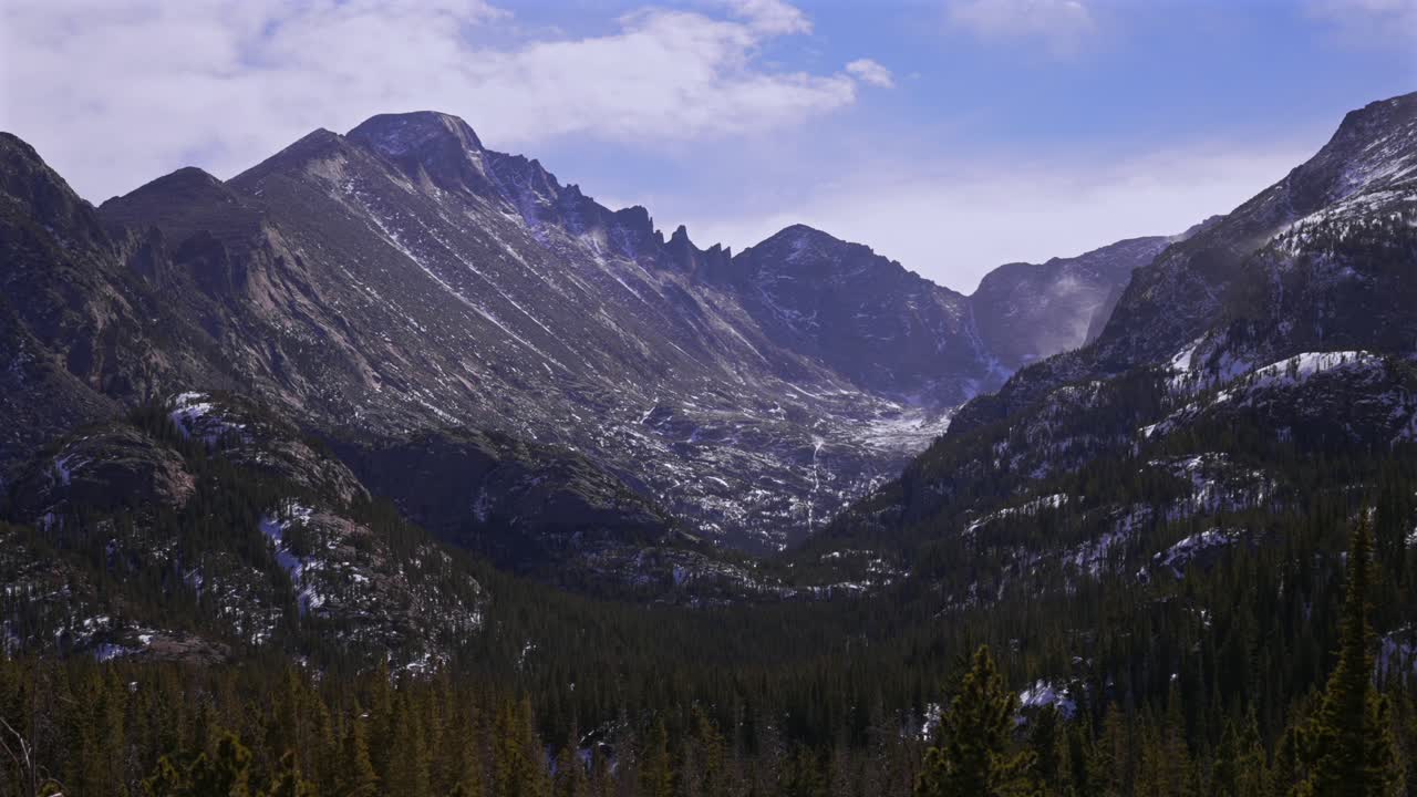 Longs Peak in inverno, Parco Nazionale delle Montagne Rocciose, Colorado. Paesaggio naturale con cielo blu soleggiato e nuvole. Veduta dei laghi Bear, Dream ed Emerald dal sentiero, neve portata dal vento, alberi. Ripresa statica del sentiero escursionistico.