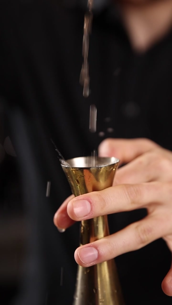 Ripresa al rallentatore di liquido versato in un jigger dorato