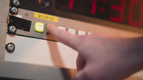 close-up shot of finger pressing button on electronic control panel, green light indicating activation, with red timer displayed. broadcast studio control in action