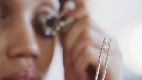 Biracial-female-worker-inspecting-jewellery-with-magnifying-glass-in-studio-in-slow-motion