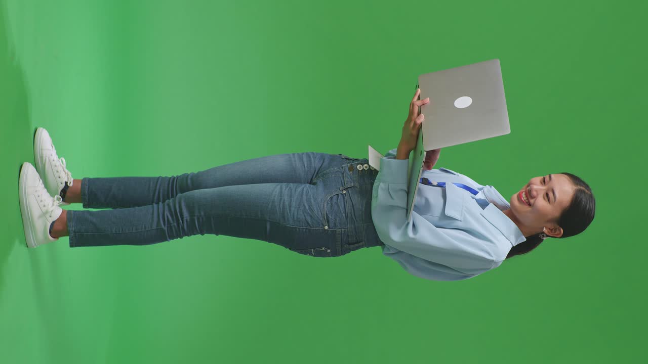 vista lateral de cuerpo completo mujer de negocios asiática usando computadora portátil en fondo de pantalla verde en el estudio
