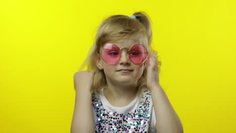 Child-smiling,-looking-at-camera.-Girl-tourist-in-pink-sunglasses-posing-on-yellow-background