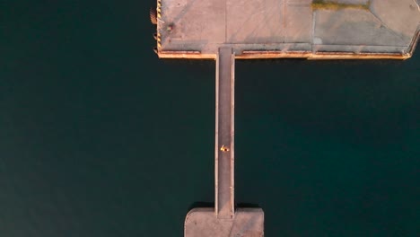 top down aerial drone view of male walking across stone bridge in ocean harbor