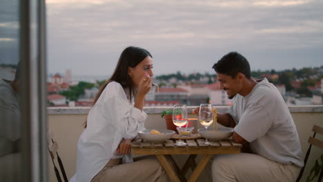 una pareja de amor disfrutando de la comida en el balcón de la vista de la ciudad al atardecer. una pareja celebrando verticalmente