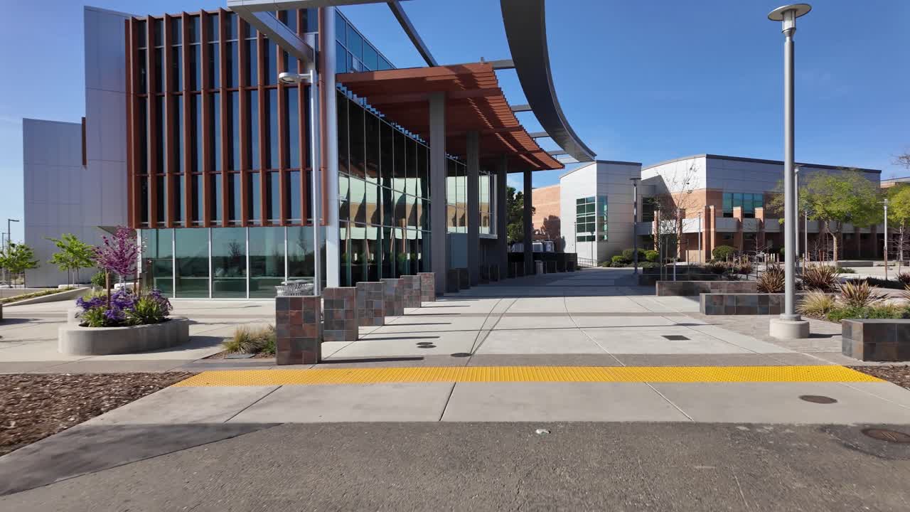 Toma en primera persona caminando hacia atrás desde la entrada de arquitectura moderna del Folsom Lake College en Folsom, California, en un día soleado y brillante con un cielo azul despejado