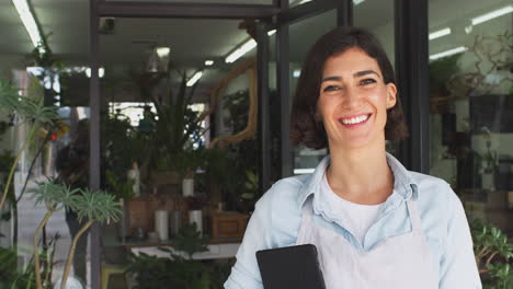 retrato de una mujer propietaria de floristerías con una tableta digital de pie en la puerta rodeada de plantas