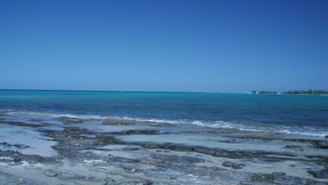 Hermosas-Olas-De-Agua-Del-Océano-En-La-Costa-Rocosa-Con-Una-Isla-En-El-Fondo