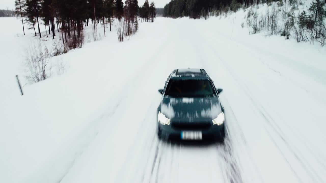 un coche eléctrico pasa bajo un dron en una carretera nevada en el círculo polar ártico