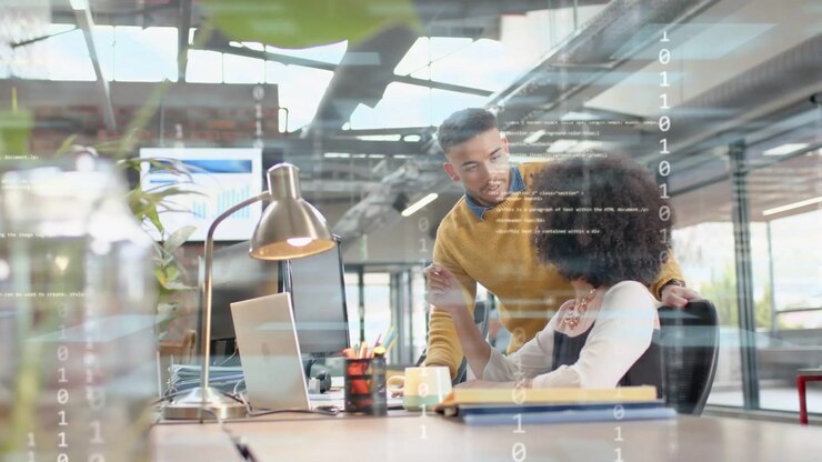 Seated woman pointing laptop as standing man leaning over causing overlay clarifying office chart