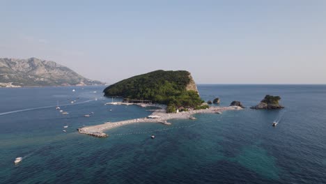 Sveti-Nikola-Island,-Budva,-Montenegro-from-above-ocean-as-boats-drive-over-reef