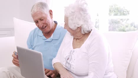una pareja de adultos mayores sonrientes usando una computadora portátil