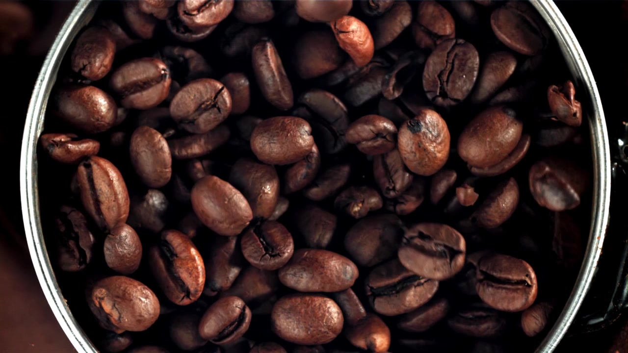 Ristede kaffebønner falder ned i en beholder i slowmotion