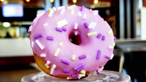 sprinkle donut foreground close up zoom in with bokeh people background preparing and ordering dessert doughnut bright pink magenta with yellow white purple edible confetti