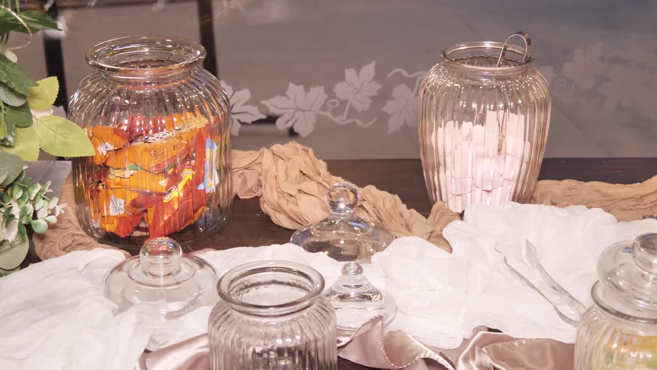 A rustic candy bar setup with clear glass jars holding assorted sweet treats, including a jar of pink marshmallows