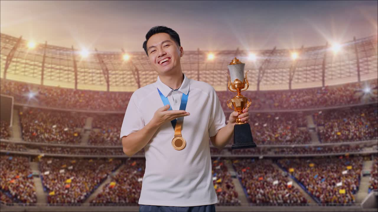 금메달을  아시아 남자가 손에 금 트로피를 가리키며 미소 짓고 경기장에서 첫 우승자로 자랑스럽게 승리합니다.