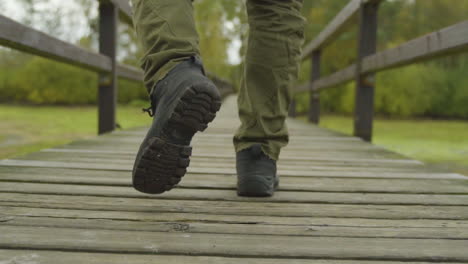 Hiker-walking-through-wooden-bridge-in-cloudy-woodland,-adventure-in-the-forest-for-exploration